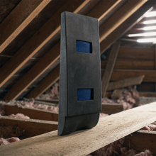 The hardened shell standing on an attic joist, spanning knee to shin, with its two blue webbing straps